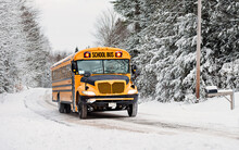 Yellow school bus travelling down a snowy country road