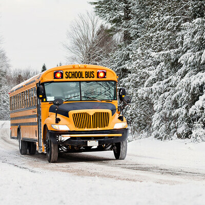 Yellow school bus travelling down a snowy country road