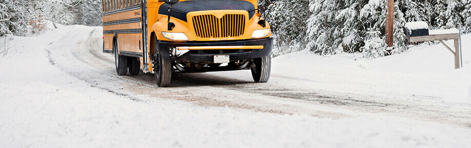 Yellow school bus travelling down a snowy country road