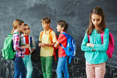 Lonely schoolgirl on background of her classmates having talk