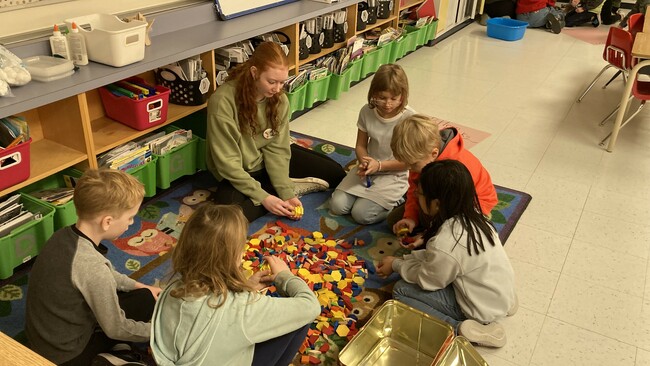 Students sitting on a classroom floor using manipulatives to practice counting